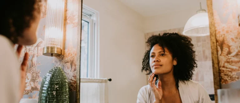 een mooie vrouw onderzoekt haar huid in een badkamerspiegel