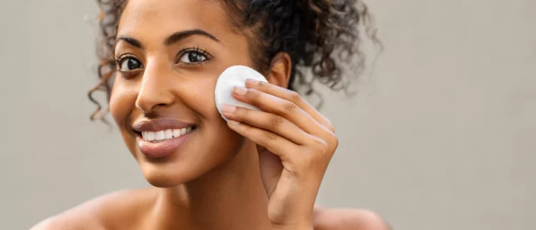 jovem afro-americana bonita tirando a sua maquilhagem com esponja de algodão esponja sorridente rapariga limpando o rosto com almofada de algodão isolada sobre fundo jovem mulher negra limpando o rosto, diariamente saudável ser