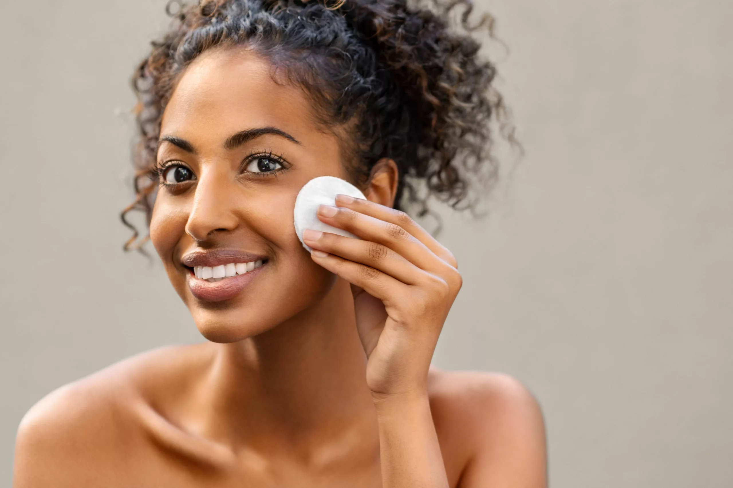 jeune femme afro-américaine se démaquillant avec une éponge en coton fille souriante se nettoyant le visage avec un coton isolé sur fond noir jeune femme se nettoyant le visage, être sain au quotidien