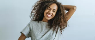 ritratto di donna con capelli afro che sorride con sfondo muro bianco