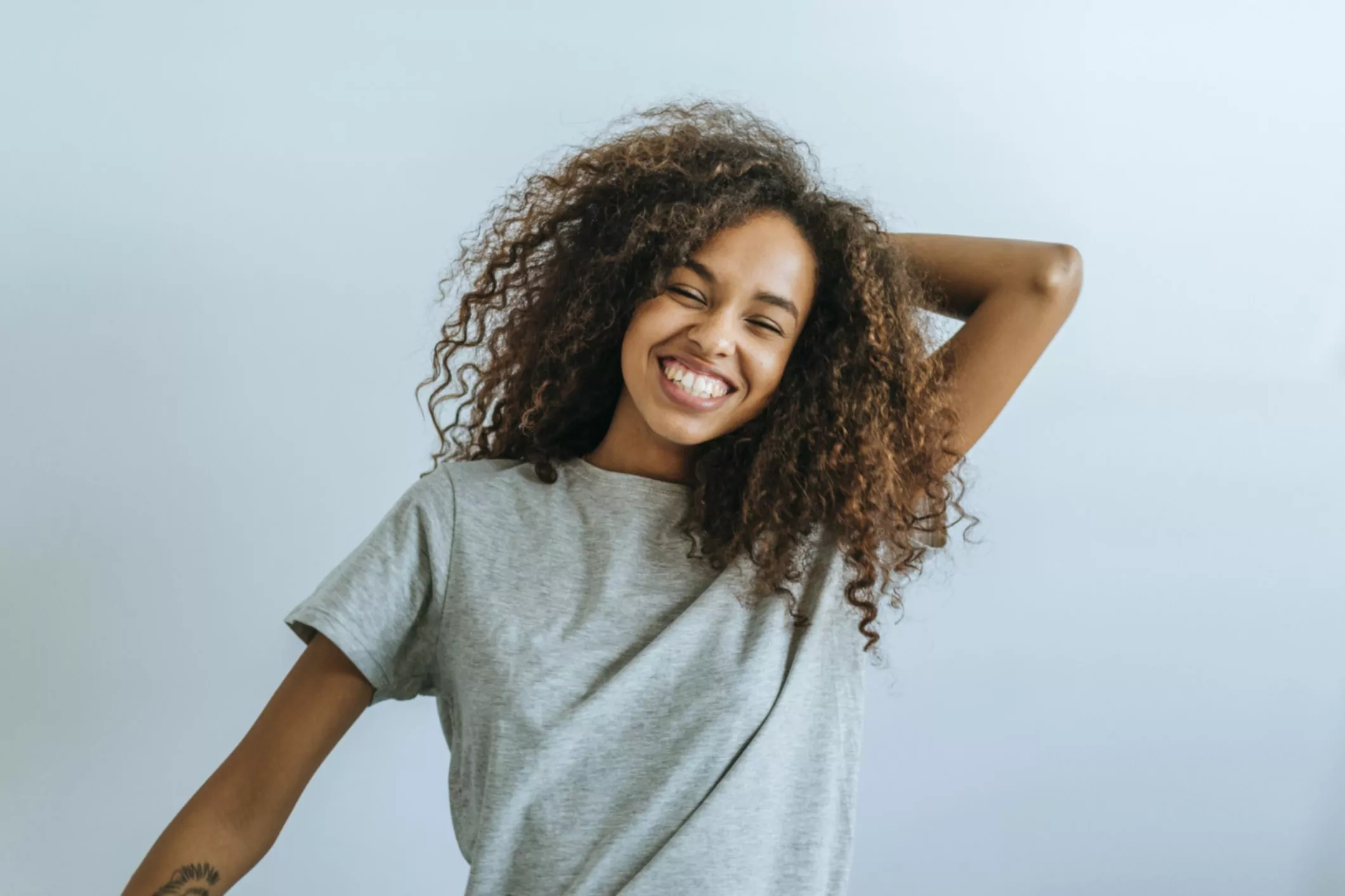 portret van vrouw met afro haar glimlachend met witte muur achtergrond